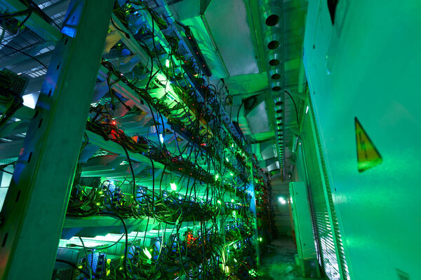 Bitcoin miners in large farm. ASIC mining equipment on stand racks mine cryptocurrency in steel container. Blockchain techology application specific integrated circuit datacenter. Server room lights.