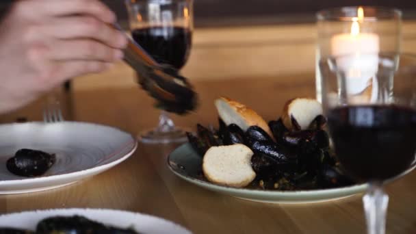 豪华餐厅的游客们吃着美味的新鲜贻贝，这些贻贝用红葡萄酒盛在大盘上。人们在咖啡店里把贻贝放在盘子里.盘子里的传统的中间主义菜肴.海鲜小吃. — 图库视频影像
