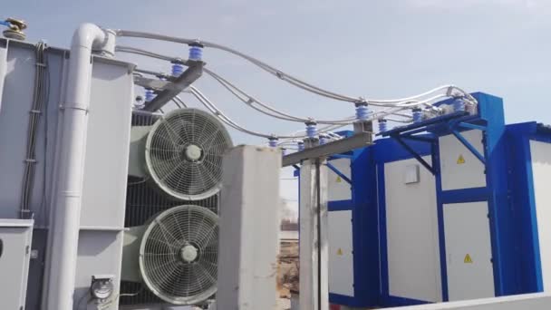 Güneşli bir günde elektrik dağıtım istasyonunda kablolu güç transformatörü. Modern trafoda aktif soğutma vantilatörü. Yalıtıcılarda yüksek voltajlı güç hattı. — Stok video