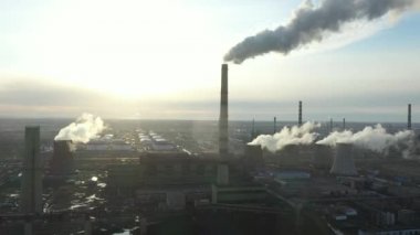 Termik santralin hava görüntüsü. İnsansız hava aracı günbatımında baca dumanı borularının ve sanayi bölgesinin soğutma kulelerinin üzerinden uçuyor. Yukarıdan gelen termal elektrik üretim istasyonu hava emisyonlarını tüketiyor.