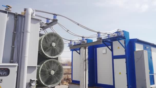 Energietransformator met kabels op elektrisch verdeelstation op zonnige dag. Actieve koelventilator op moderne transformator. Hoogspanningsleiding op isolatoren. — Stockvideo