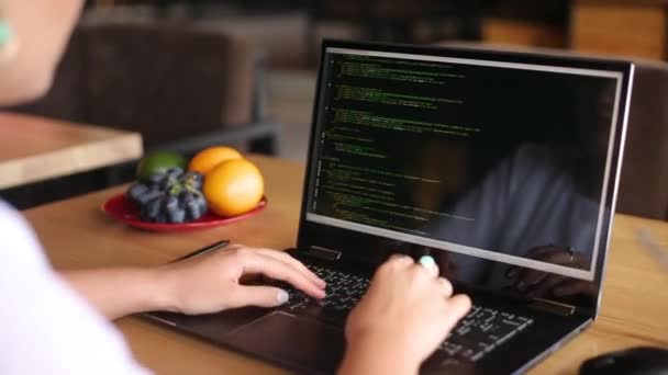 Rückansicht über die Schulter einer Entwicklerprogrammiererin mit Laptop. Programmcode und Skriptdaten auf dem Bildschirm. Junge Freiberuflerin arbeitet an Projekt im Café. — Stockvideo