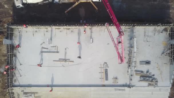 Aerial of concrete boom pump grue arm truck with outriggers couling building mixture into a formwork. Les ouvriers de la construction versent les murs en béton armé de la tribune. Vue d'en haut. — Video