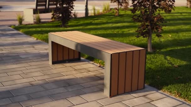 Bancs en bois modernes sur la pelouse dans le parc. Nouveau banc élégant dans la zone de loisirs de la ville au lever ou au coucher du soleil. Urbanisme thème espace public aménagement paysager. Personne sur le trottoir de la rue vide. — Video