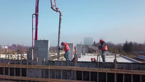 Aerial of concrete boom pump grue arm truck with outriggers couling building mixture into a formwork. Les ouvriers de la construction versent les murs en béton armé de la tribune. Vue d'en haut. — Video