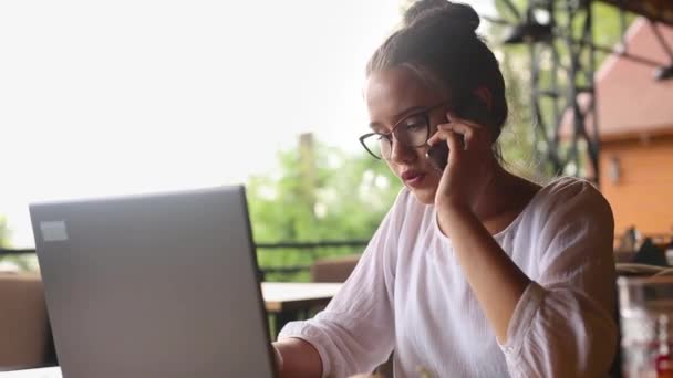 Blandet race business kvinde distraheret fra arbejde på den bærbare computer via telefonopkald. Freelancer kvinde taler på mobiltelefon, mens sms 'e på bærbare tastatur på arbejdspladsen. Multitasking koncept. – Stock-video