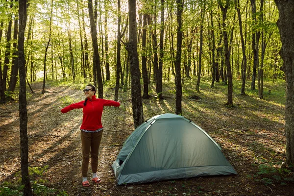 Pretty tourist girl doing morning work-out near  tent in wild forest — 스톡 사진