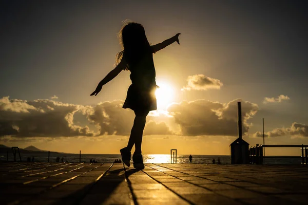 Fröhlich tanzendes kleines Mädchen, das den Sonnenuntergang am Strand beobachtet — Stockfoto