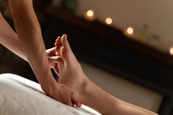 Massagista fazendo uma massagem nos pés com velas no fundo — Fotografia de Stock