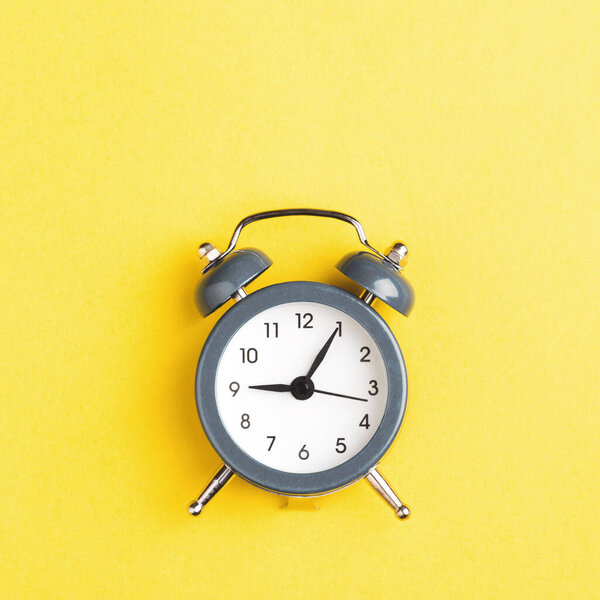 Серый будильник на желтом фоне.