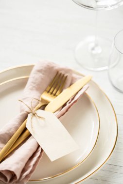 Altın kenarlı tabaklar ve beyaz masada etiketli altın çatal bıçak..