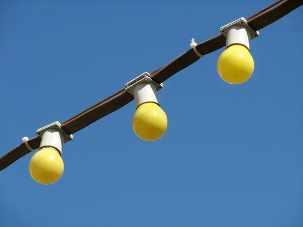 Drei gelbe Glühbirnen auf dem Draht auf blauem Himmelshintergrund — Stockfoto