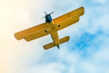 İki pilotlu sarı uçak mavi bulutlu gökyüzünde cesurca dönüş yapıyor.