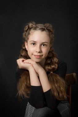 Portrait of a beautiful  blond girl with wavy long hair, on a black background, waist-deep, with a hand touching her face, vertical