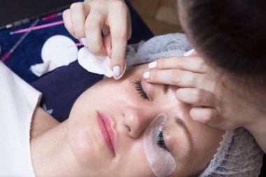 Gözleri kapalı bir kadın uzanmış yatarken, güzellik uzmanları rahat bir salon ortamında dikkatlice kirpik takıyor..