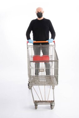 Ağız korumalı ve eldivenli bir adam beyaz arka planda izole edilmiş bir alışveriş arabasını itiyor.