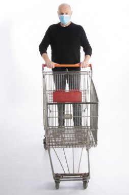 Ağız korumalı bir adam beyaz arka planda izole edilmiş bir alışveriş arabasını itiyor.