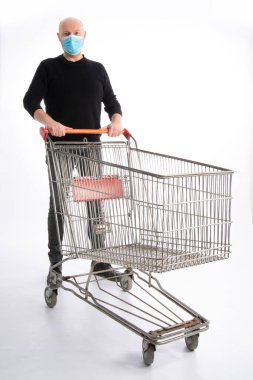 Ağız korumalı bir adam beyaz arka planda izole edilmiş bir alışveriş arabasını itiyor.