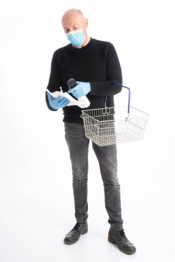 Ağız korumalı ve eldivenli bir adam beyaz arka planda izole edilmiş bir alışveriş arabasını temizlemeye başlıyor.