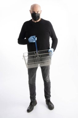 Ağız korumalı ve eldivenli bir adam beyaz arka planda izole edilmiş bir alışveriş sepeti tutuyor.