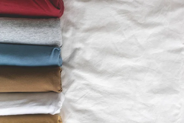 Färgglada rullar av t-shirt på den vita sängen. — Stockfoto