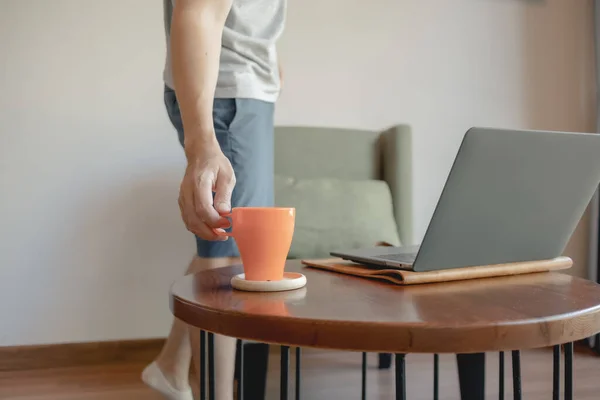 Man is picking up coffee cup while working on his laptop.