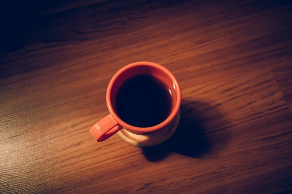 昏暗灯光下木制地板上的橙色热咖啡杯. — 图库照片