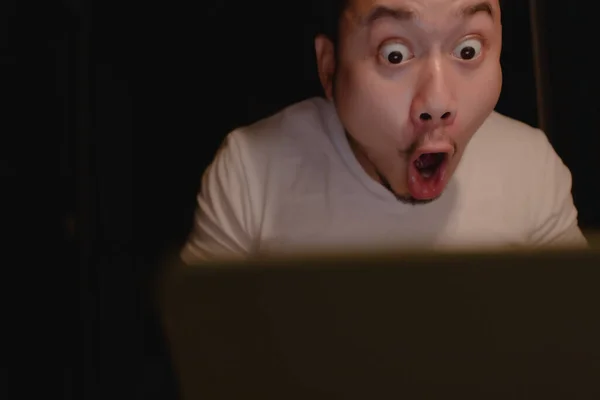 Schockiertes und überraschtes Gesicht eines Asiaten, der nachts Laptop benutzt. — Stockfoto