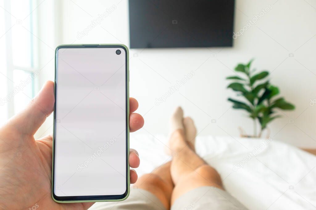 First person view of man using smartphone while on the bed.