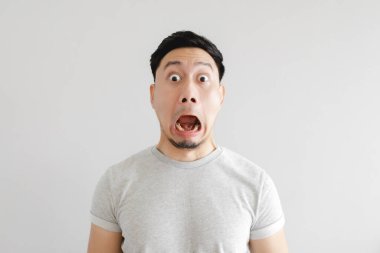 Gri tişörtlü ve gri arka planlı adamın şok olmuş yüzü.