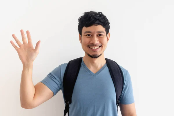 Man in blue t-shirt with backpack is waving hand on isolated background. — Stock Photo, Image