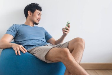 Mutlu adam akıllı telefon kullanırken oturup fasulye torbasının üzerinde rahatlıyor..
