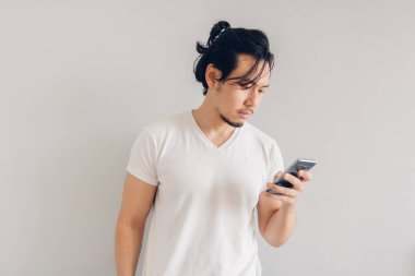 Beyaz tişörtlü ciddi bir adam gri arka planda akıllı telefon kullanıyor..