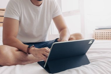 Adam yatak odasında tablet ve kahveyle çalışıyor. Evden çalışma kavramı.