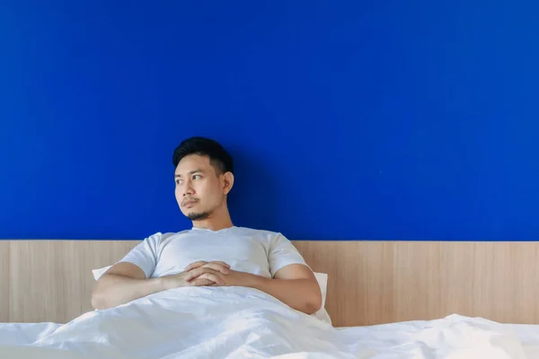 Hombre serio y gruñón se despierta en la cama en el fondo del espacio azul. — Foto de Stock