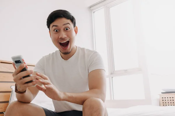 Wow face of man surprised while look at the smartphone in his apartment.