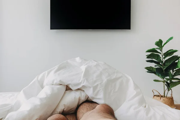 En person som sover på sängen och tittar på tv. Begreppet vistelse hemma. — Stockfoto