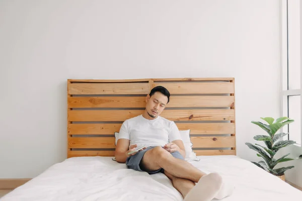 손에 전화기를 들고 침대에서 잠 들어 있는 아시아 남자. — 스톡 사진