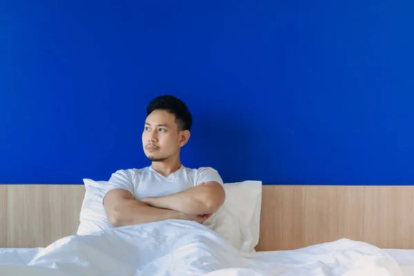 우울하고 진지 한 남자가 침대에서 일어나 파란 우주 배경 위에서. — 스톡 사진