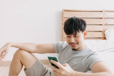 Dairesinde dinlenirken akıllı telefon kullanan mutlu bir adam. Evde kal..