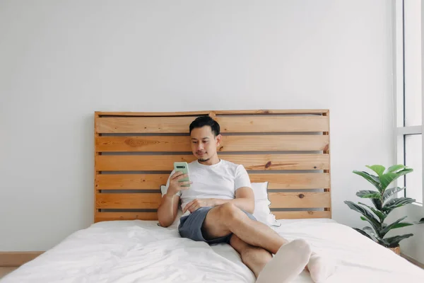 Pria Asia yang bahagia merasa santai dengan smartphone di tempat tidurnya. — Stok Foto