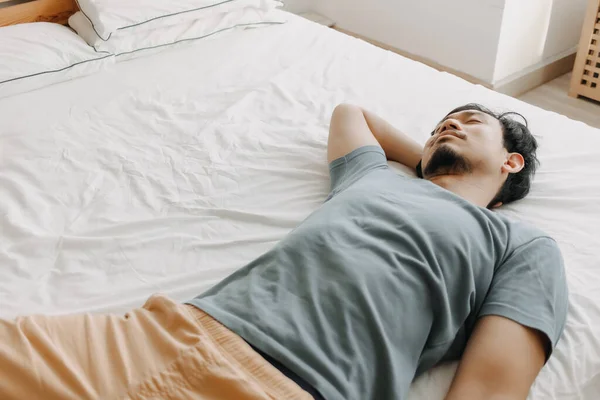 Ο κουρασμένος άντρας είναι ξαπλωμένος στο κρεβάτι καθώς ξεμένει από ενέργεια.. — Φωτογραφία Αρχείου