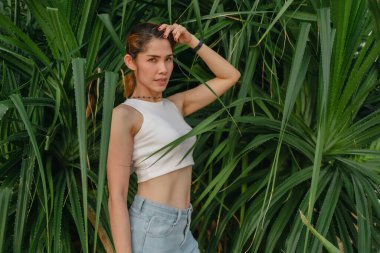 Güzel bir kadın yaz konseptinde fotoğraf için yeşil palmiye çalılığında poz verir..