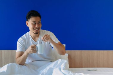 Adam sabah kahvesini mavi perdeli yatakta içiyor..