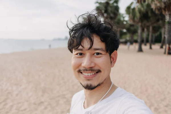 Un uomo felice si fa un selfie con una palma sulla spiaggia. Concetto viaggio estivo. — Foto Stock