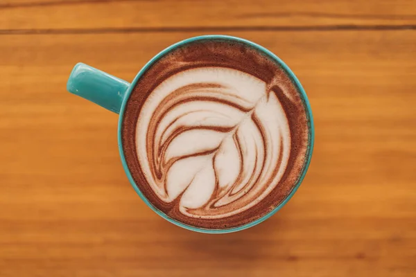 Cangkir kopi biru dengan seni latte penuh di atas meja kayu. — Stok Foto