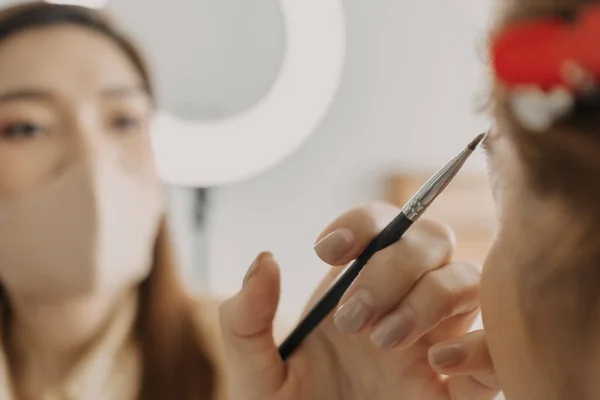 Woman makeup artist is at work and wearing makeup on her model.