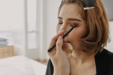 Makyaj sanatçısı müşteri gözlerine makyaj yapıyor.