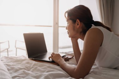 Yatakta dizüstü bilgisayarla çalışan bir kadın. Otelden çalışma kavramı.