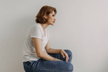 Beyaz tişörtlü, kot pantolonlu bir kadın dairesinde rahatlıyor..